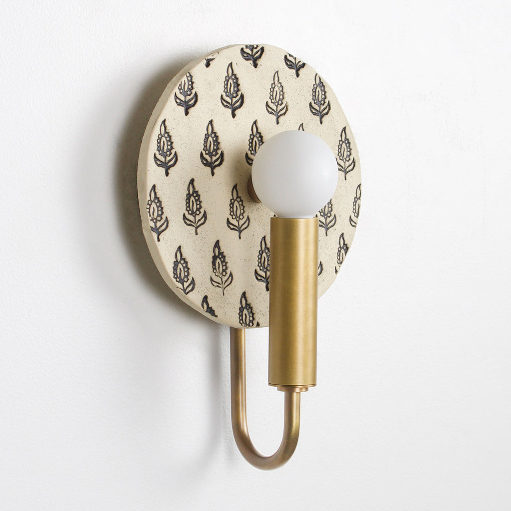 Edith ADA Sconce shown in Heirloom Brass with a Black and Cream Floral ceramic backplate.